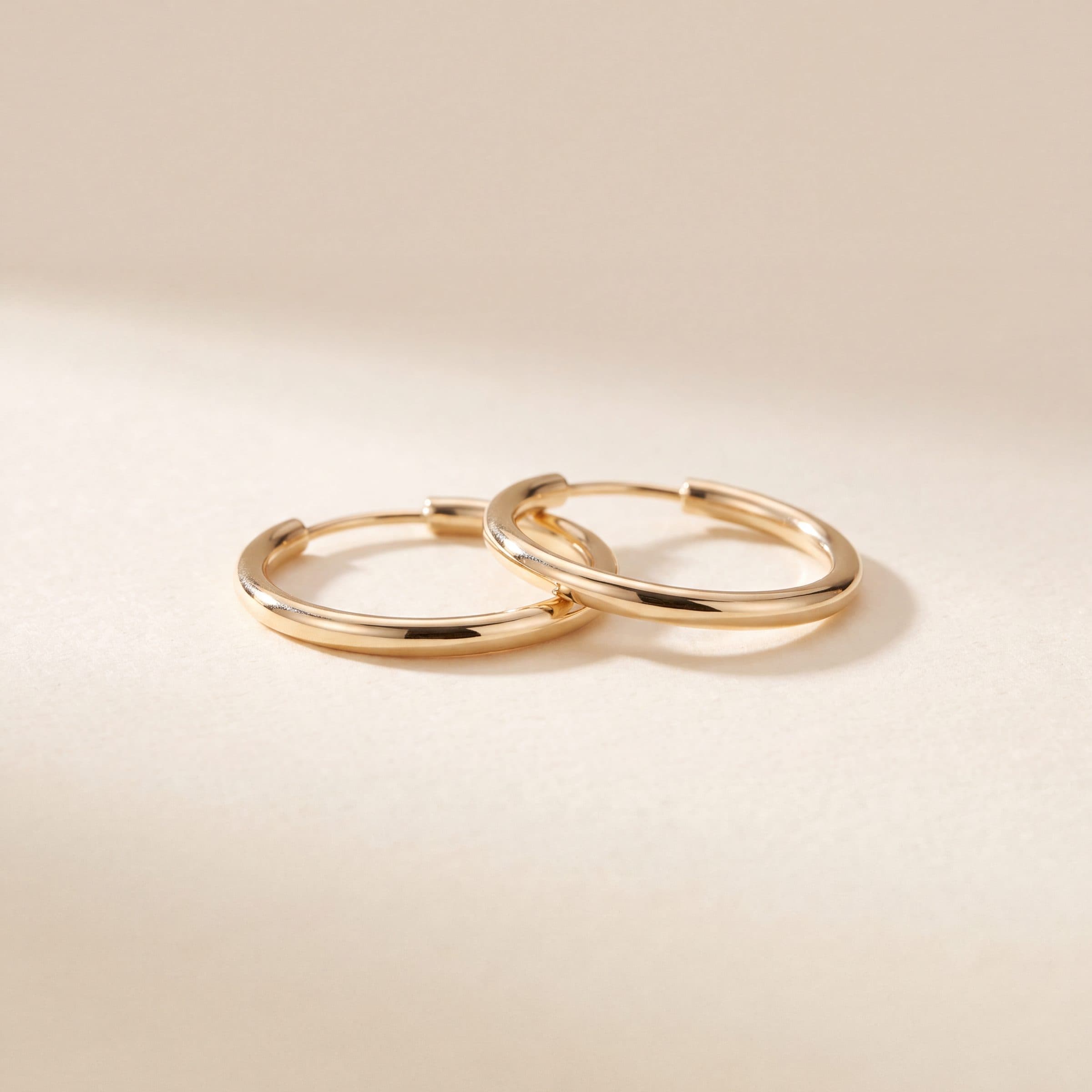 Minimalist 18K gold hoop earrings photographed against a neutral background