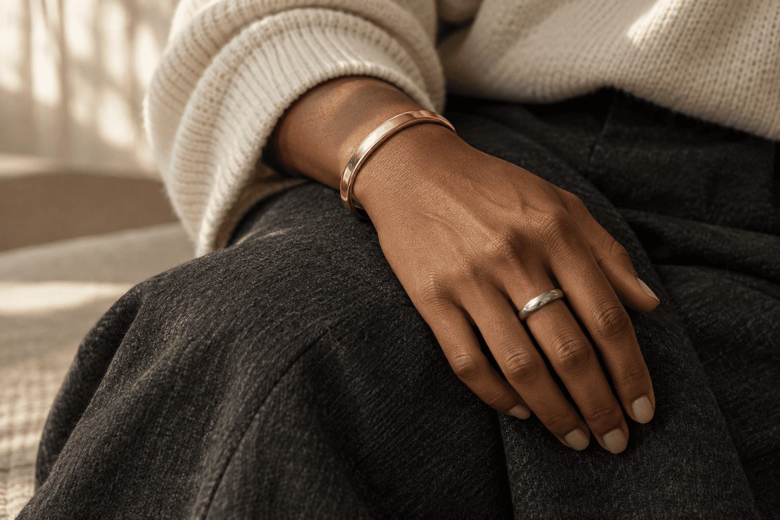 A gold cuff and a simple silver ring worn together with cream knitwear and charcoal trousers
