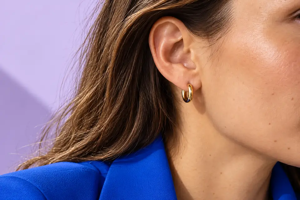 Small gold hoop worn with tucked-back brown hair, a cobalt collar and a lilac backdrop