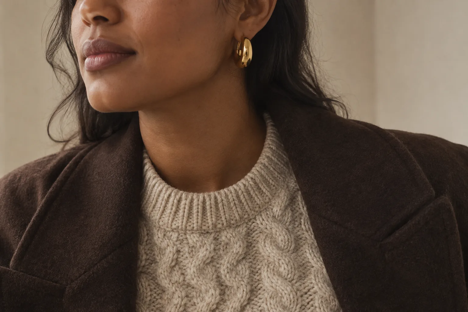A gold hoop worn with an oatmeal cable-knit sweater and an open brown wool jacket